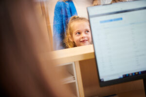 Shot from a receptionist’s point of view on a young girl at the counter, smiling.