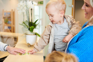 A toddler being carried by a woman and handing over their insurance card to the receptionist.