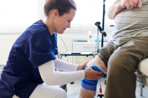 A medical assistant bandaging the knee of an elderly patient.