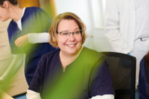 Shot through a plant over the desk at a medical assistant happily smiling.
