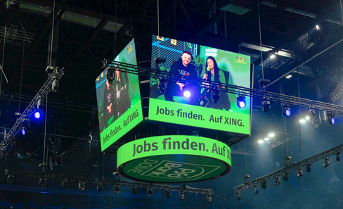An LED cube in a sports hall showing an interview happening, below an LED circle with the marquee text “Jobs finden. Auf XING.”