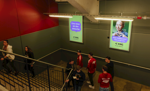 In a staircase oÏ a sports hall there are two digital OOH displays with various stages of the animated XING jobs campaign ads.”
